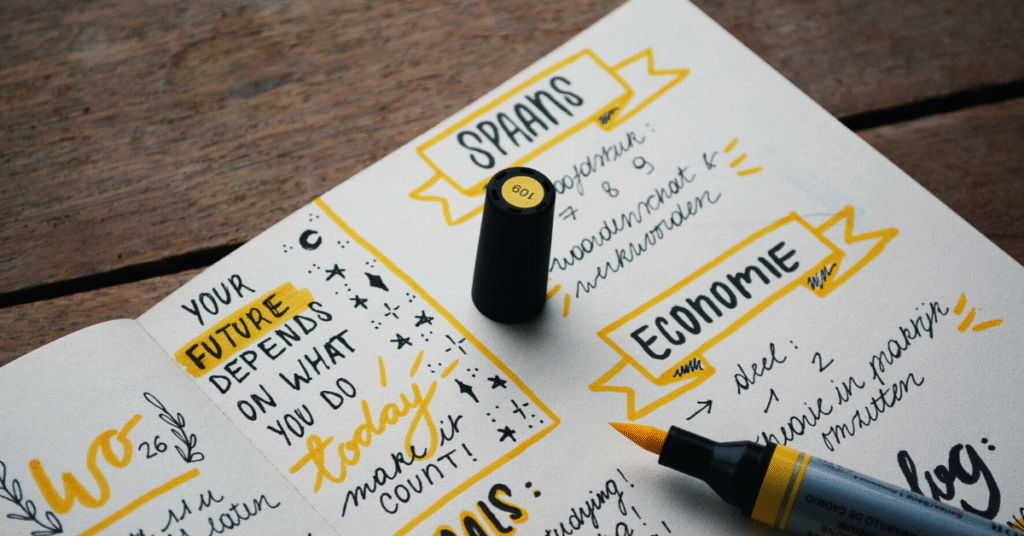 An open notebook on a wooden surface featuring hand-drawn headers in yellow banners