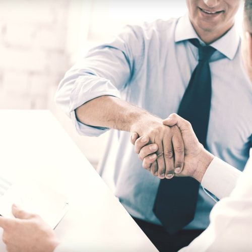 A close-up of two men in office attire shaking hands across a desk.